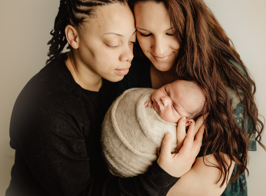 A parent and partner holding their swaddled newborn baby close
