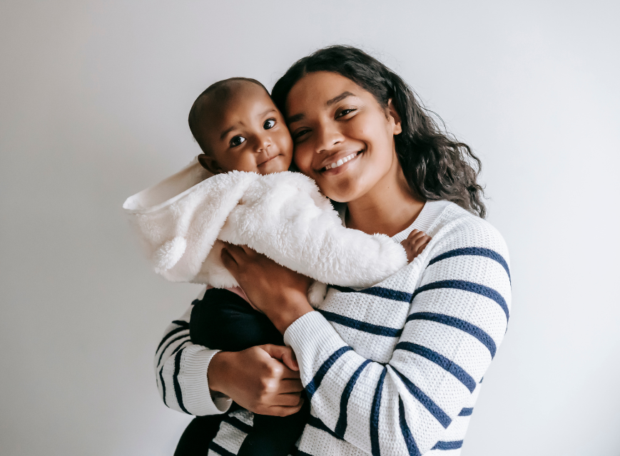 A smiling mother cuddling her baby wrapped in a soft white blanket